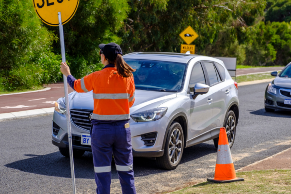 AusQ Training learner holding a slow sign and directing vehicles during practical traffic control training on a roadside worksite.