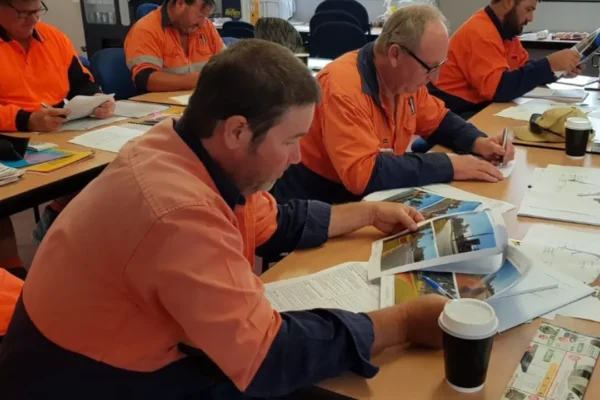 AusQ Training learners wearing high-visibility work shirts reviewing training materials and manuals during a classroom-based traffic management course.