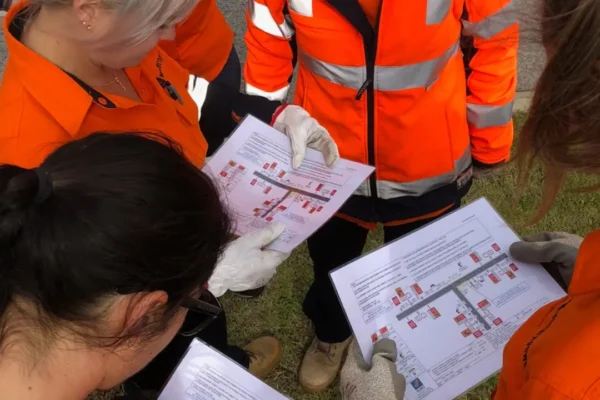 AusQ Training learners wearing high-visibility safety gear reviewing a Traffic Management Plan (TMP) during practical training session.
